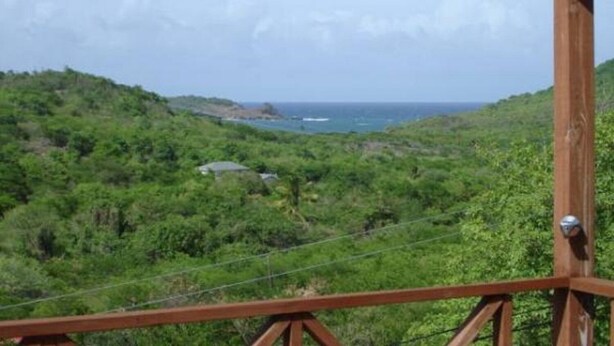 A wooden structure with a metal railing, overlooking a coastal landscape with greenery and a view of the sea. - Sea view apartment with Quietness and relaxation. (Gros Islet)