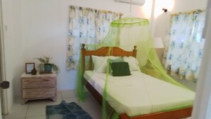 A bedroom with a wooden bed, a nightstand, a small table, and a green canopy. - Sea view apartment with Quietness and relaxation. (Gros Islet)