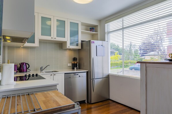 A modern kitchen with white cabinetry, a stainless steel refrigerator, and a window with blinds.