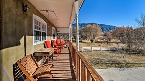 Una terraza de madera con mobiliario exterior, un porche cubierto y vistas a un paisaje montañoso.