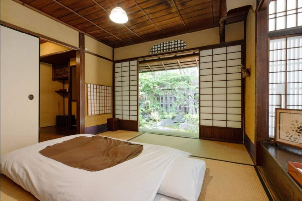 Um quarto japonês tradicional com tatames, futon, biombos shoji e vista para um jardim.