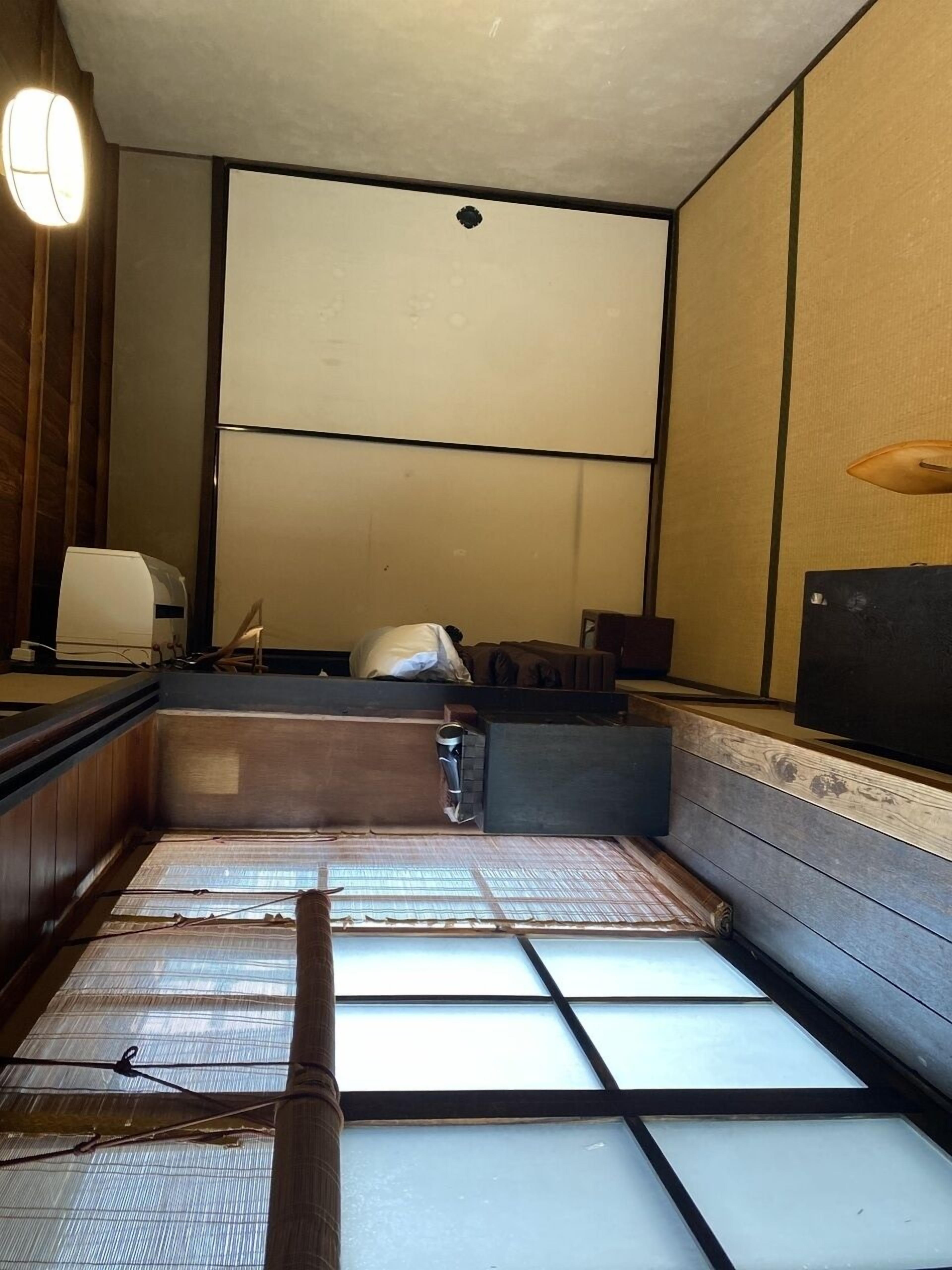 Une pièce traditionnelle avec un sol recouvert de tatamis, un futon servant de lit, une petite table et un téléviseur fixé au mur.