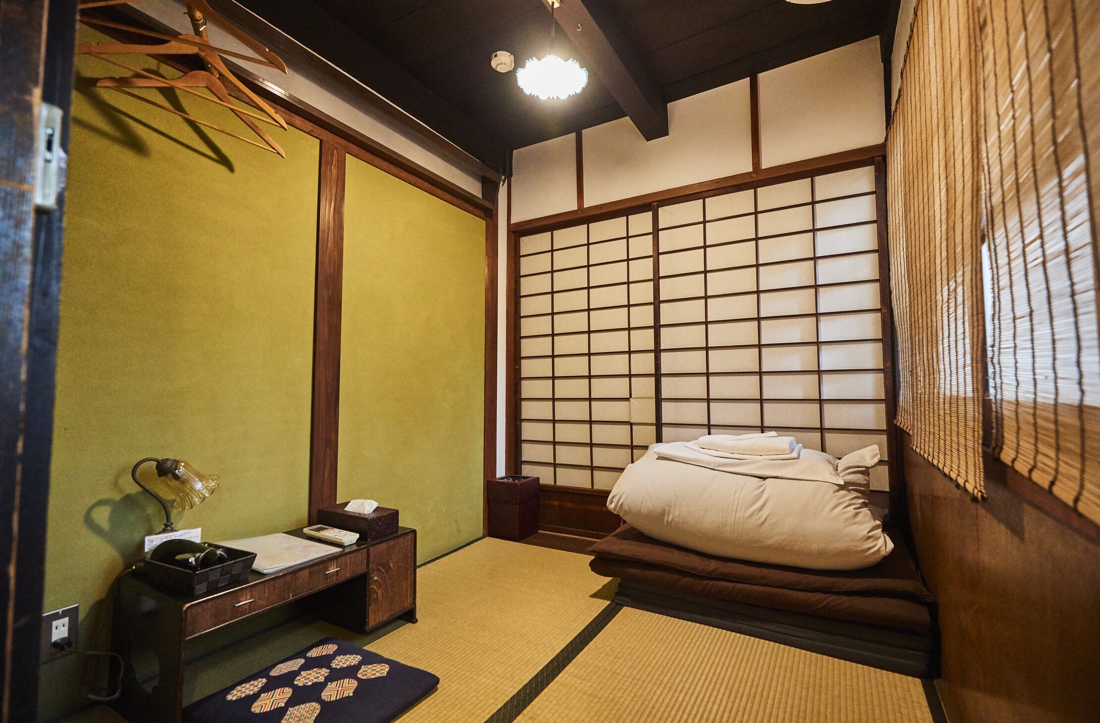 Une pièce de style japonais traditionnel, avec un sol recouvert de tatamis, un futon servant de lit, un paravent en papier de riz (shoji) et un petit bureau avec une lampe.