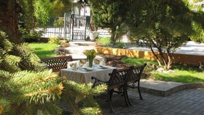 Un área de comedor al aire libre con una mesa dispuesta para dos personas, rodeada de follaje y un sendero de piedra.