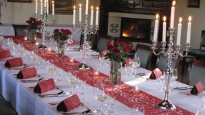 Una larga mesa de comedor dispuesta con servilletas rojas, mantel blanco y velas.