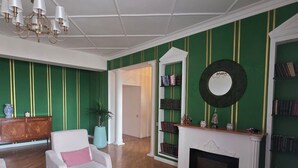 A living room with a fireplace, bookshelves, a chandelier, and a green-striped wall.
