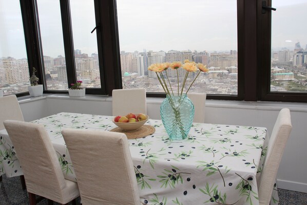 A dining area with a table set for four, a vase with flowers, and a bowl of fruit.