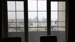 A room with a large window offering a city view. There are two chairs in the foreground.