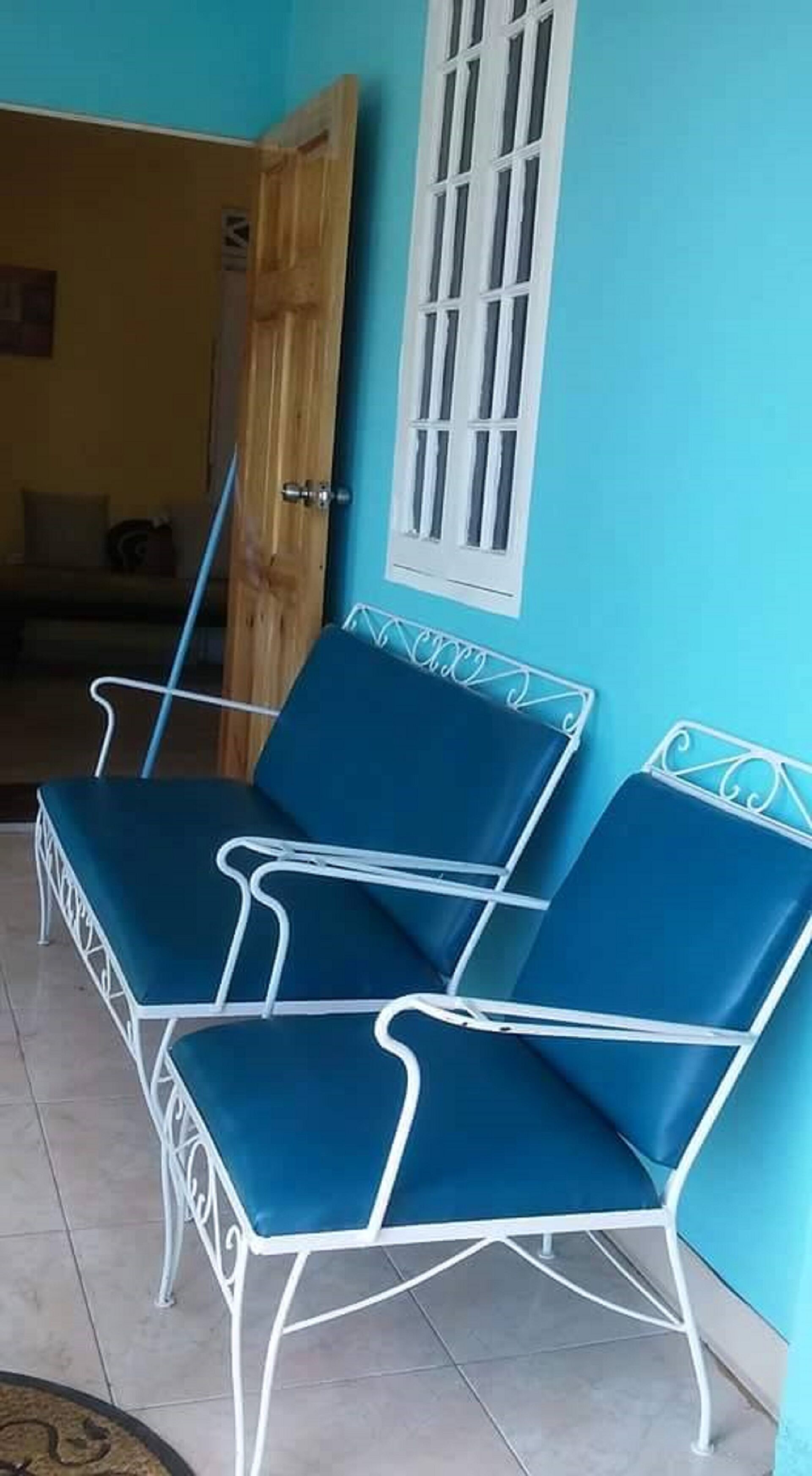 Una habitación con dos sillones azules, una puerta de madera y un ventanal con marcos blancos.