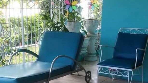 Uma área de estar coberta ao ar livre com cadeiras azuis e uma mesa de metal.