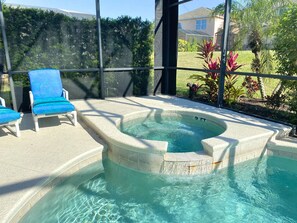 A hot tub with clear water, surrounded by a tiled deck and two blue chairs.