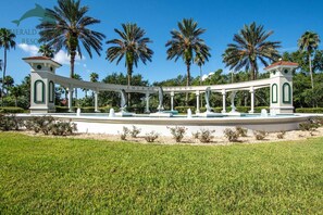 A white gazebo with green accents and a sign reading "Emerald Island" surrounded by palm trees and a well-maintained lawn.
