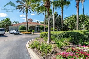 A resort with a red-tiled roof building, palm trees, and a parking area with cars.