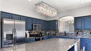 A modern kitchen with granite countertops, stainless steel appliances, and blue cabinetry. - ✦ 7BR Simba Estate ✦ 100in Home Cinema ✦ South Pool & Spa ✦ 3 Miles to Disney (Kissimmee)