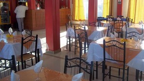 Un restaurant avec plusieurs tables et chaises, un coin bar et des rideaux jaunes.