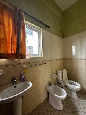 A bathroom with a sink, two toilets, a bidet, and a window with curtains.