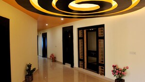 A hallway with a modern ceiling design, a potted plant, and a door with a glass panel. - Hotel Nalanda Ladakh (Leh)