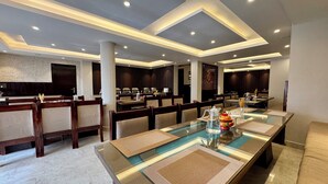 A spacious dining area with a long table, cushioned chairs, and a modern ceiling design. - Hotel Nalanda Ladakh (Leh)