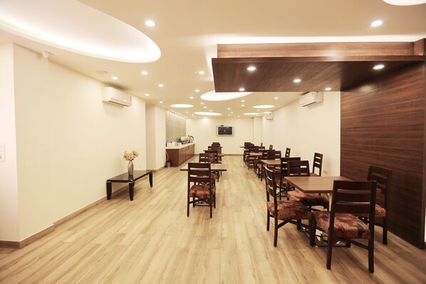 A spacious dining area with wooden tables and chairs, recessed ceiling lights, and a wooden accent wall.
