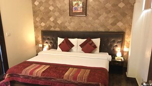 A neatly made bed with a patterned bedspread, a headboard with wall-mounted lights, and a framed picture above the bed. - Pals Inn (New Delhi)