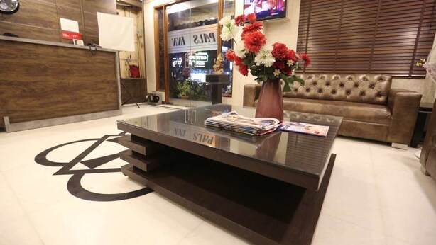 A reception area with a modern glass coffee table, a brown leather sofa, and a vase with flowers. - Pals Inn (New Delhi)