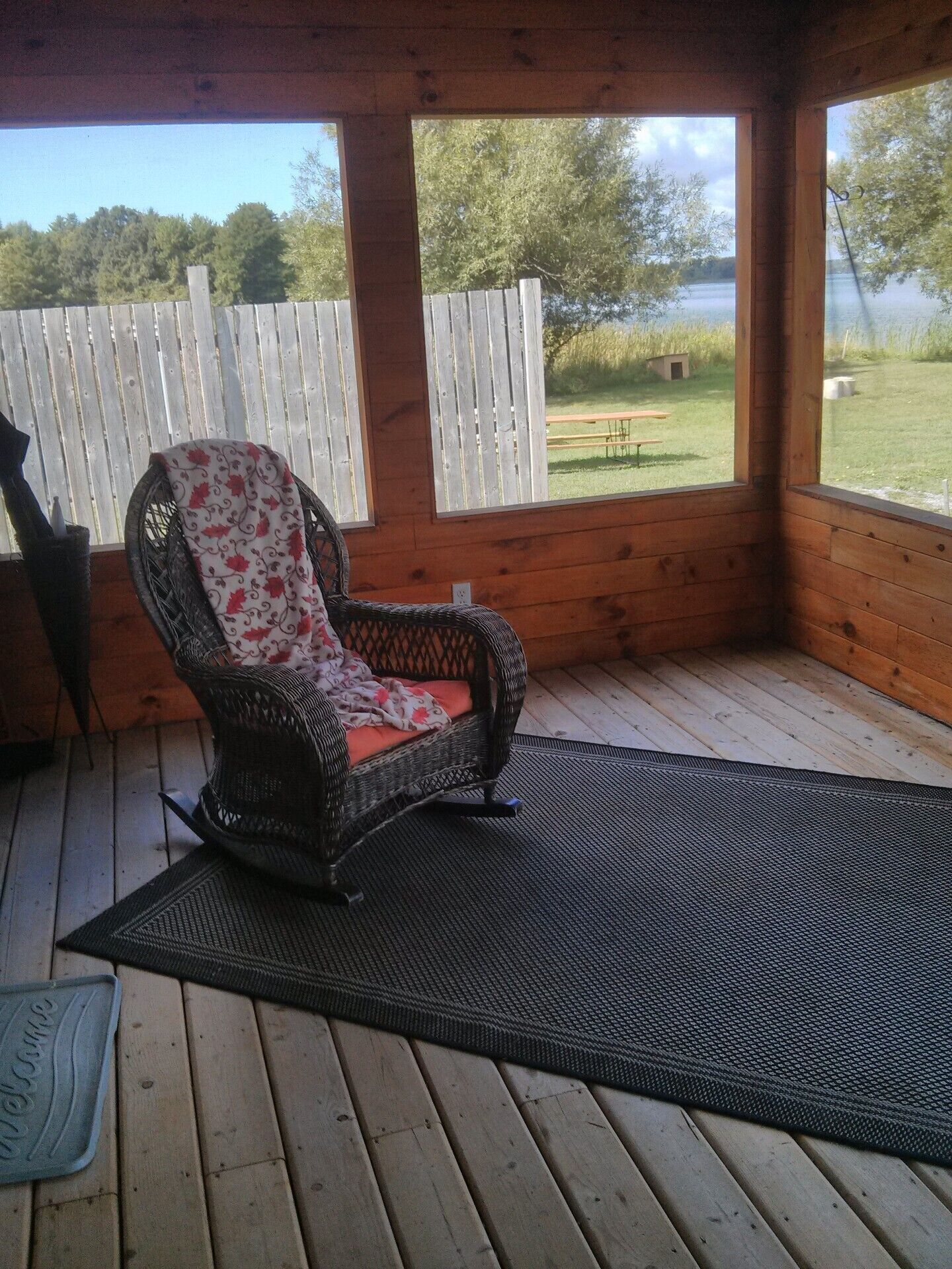 Una terraza de madera con una silla de mimbre y un felpudo.