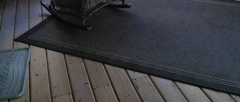 Una terraza de madera con una silla de mimbre y un felpudo.