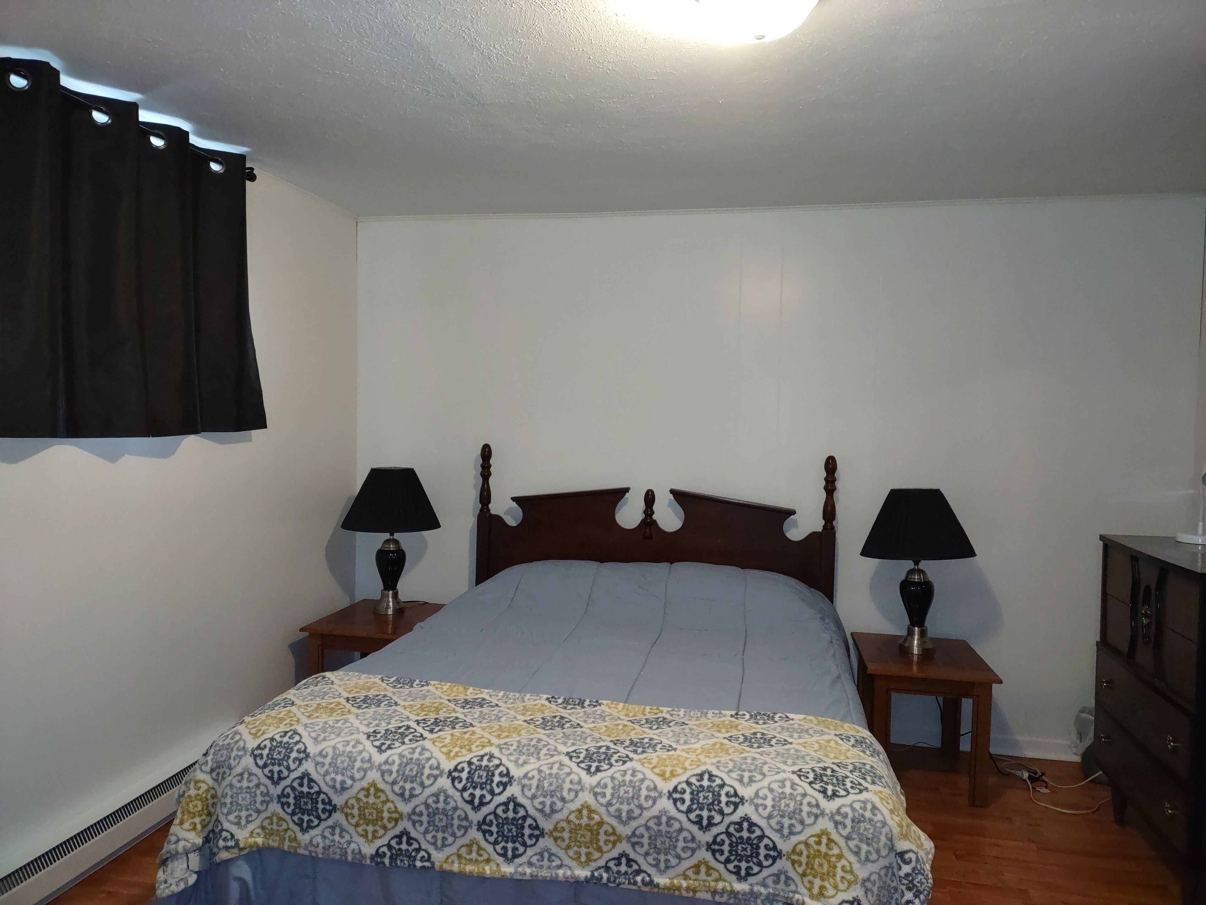 Una camera da letto con un letto, due comodini con lampade, una cassettiera e una finestra con tende.