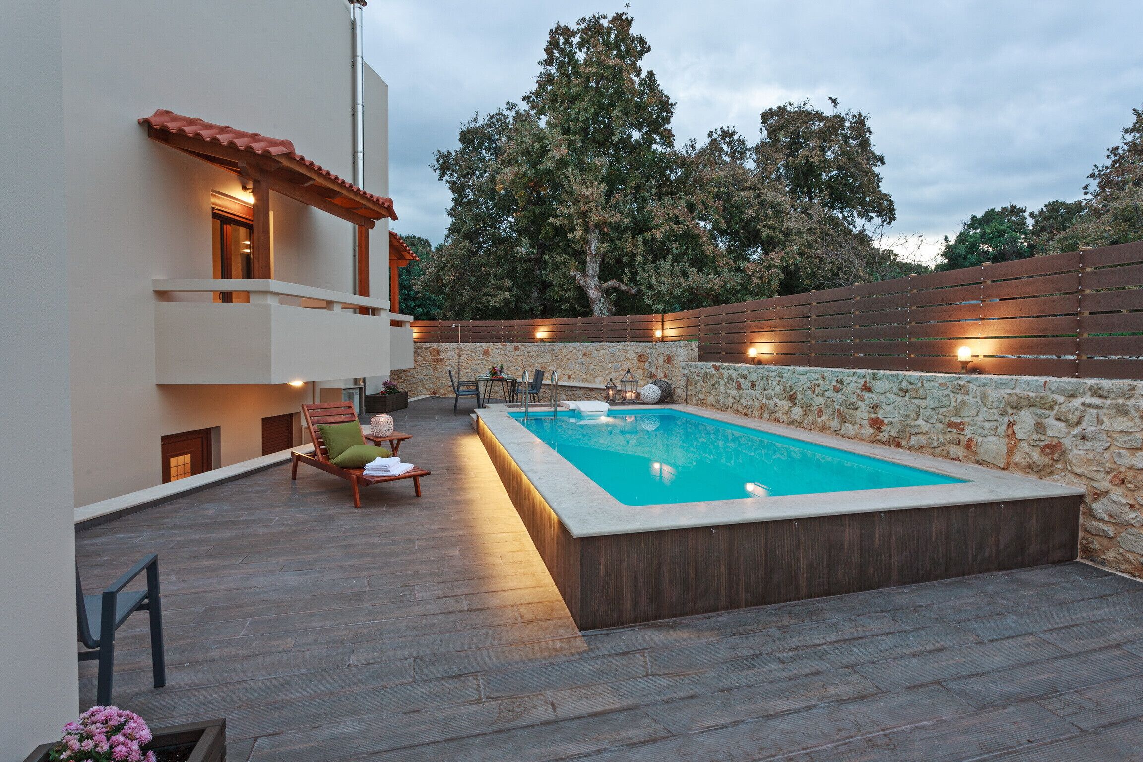 Ein Schwimmbecken mit Steinmauer, Holzterrasse und Gartenmöbeln.