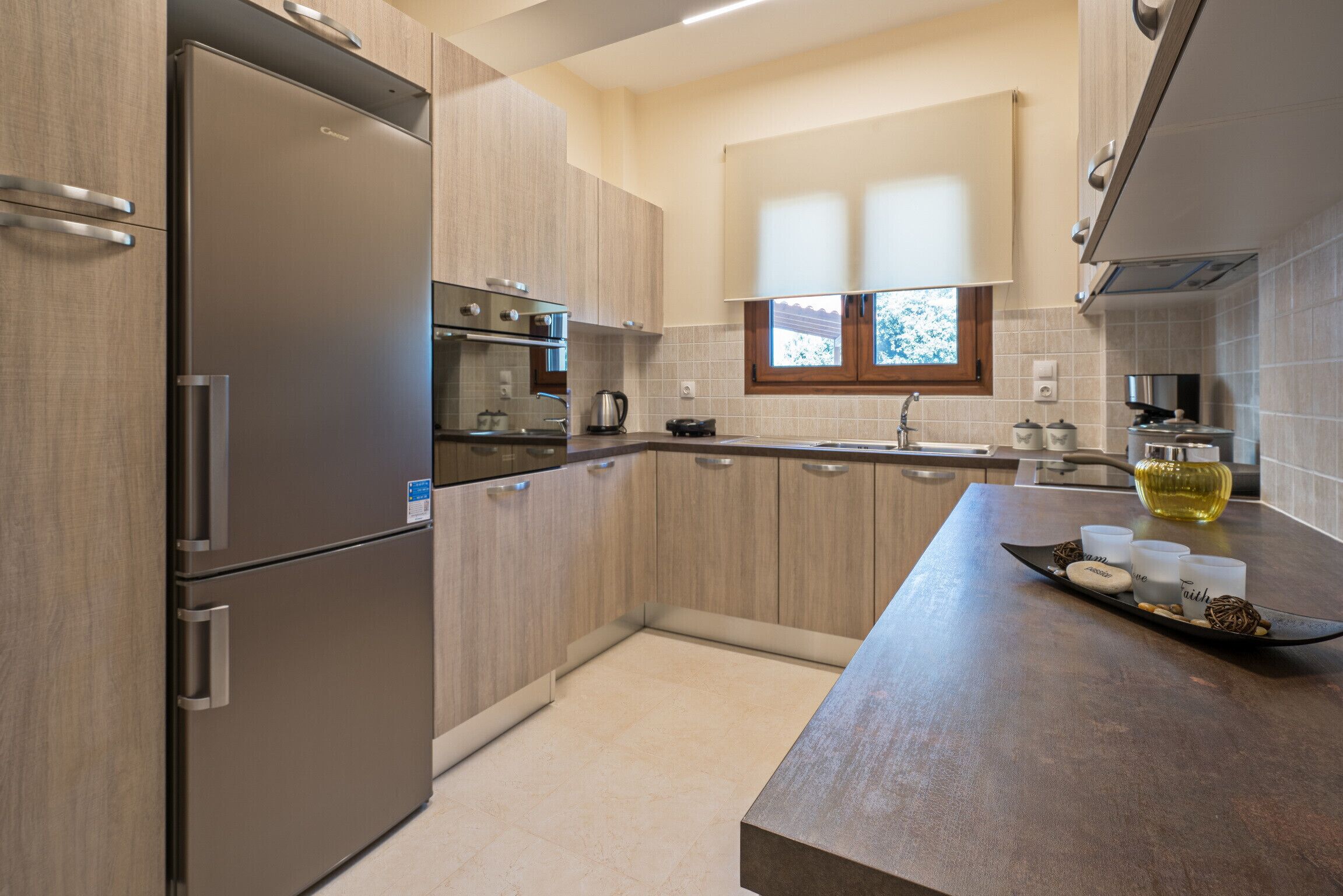 A modern kitchen with stainless steel appliances, light wood cabinetry, and a central island with a tray of items.