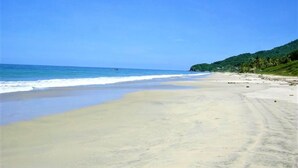 Une plage avec une eau d’un bleu limpide, un rivage sablonneux et des collines verdoyantes en arrière-plan.