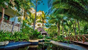 Un complexe hôtelier tropical doté d’une piscine, de palmiers et d’un chalet au toit de chaume.