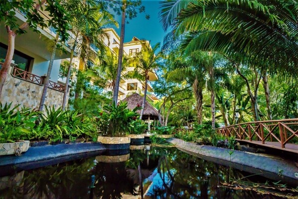 A tropical resort with a pool, palm trees, and a thatched-roof hut.