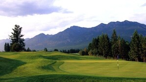 A golf course with a flagstick, surrounded by trees and mountains in the background.