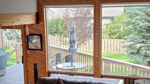 A cozy living room with a leather sofa, a wooden coffee table, and a view of a wooden deck and garden.