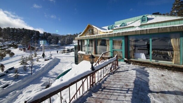 A building with a wooden staircase leading to a covered area with glass windows, surrounded by snow. - Hotel Camkar (Sarikamis)