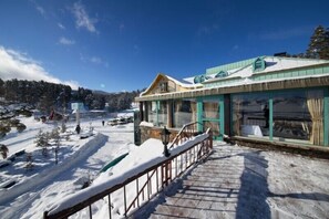 Un bâtiment doté d’un escalier en bois menant à une zone abritée avec des fenêtres en verre, le tout entouré de neige.