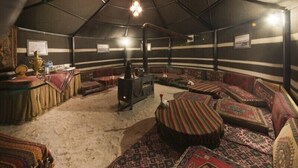 A tent-like room with a central stove, patterned cushions, and a ceiling fan. - Hotel Camkar (Sarikamis)