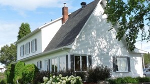 Une maison à deux étages, avec un toit à pignon, un revêtement extérieur blanc et des fondations en briques.