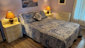Une chambre à coucher avec un grand lit, deux tables de chevet, une commode, une fenêtre avec des rideaux légers et un tableau au mur.