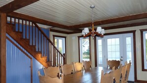 Une salle à manger avec une grande table et des chaises en bois, un escalier et un lustre.