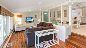 A spacious living room with a large window, a television, a sofa, a coffee table, and a dining area with chairs. - Single Level Home on Cape San Blas, Pet Friendly with Great Views - Cape Haus (Cape San Blas)