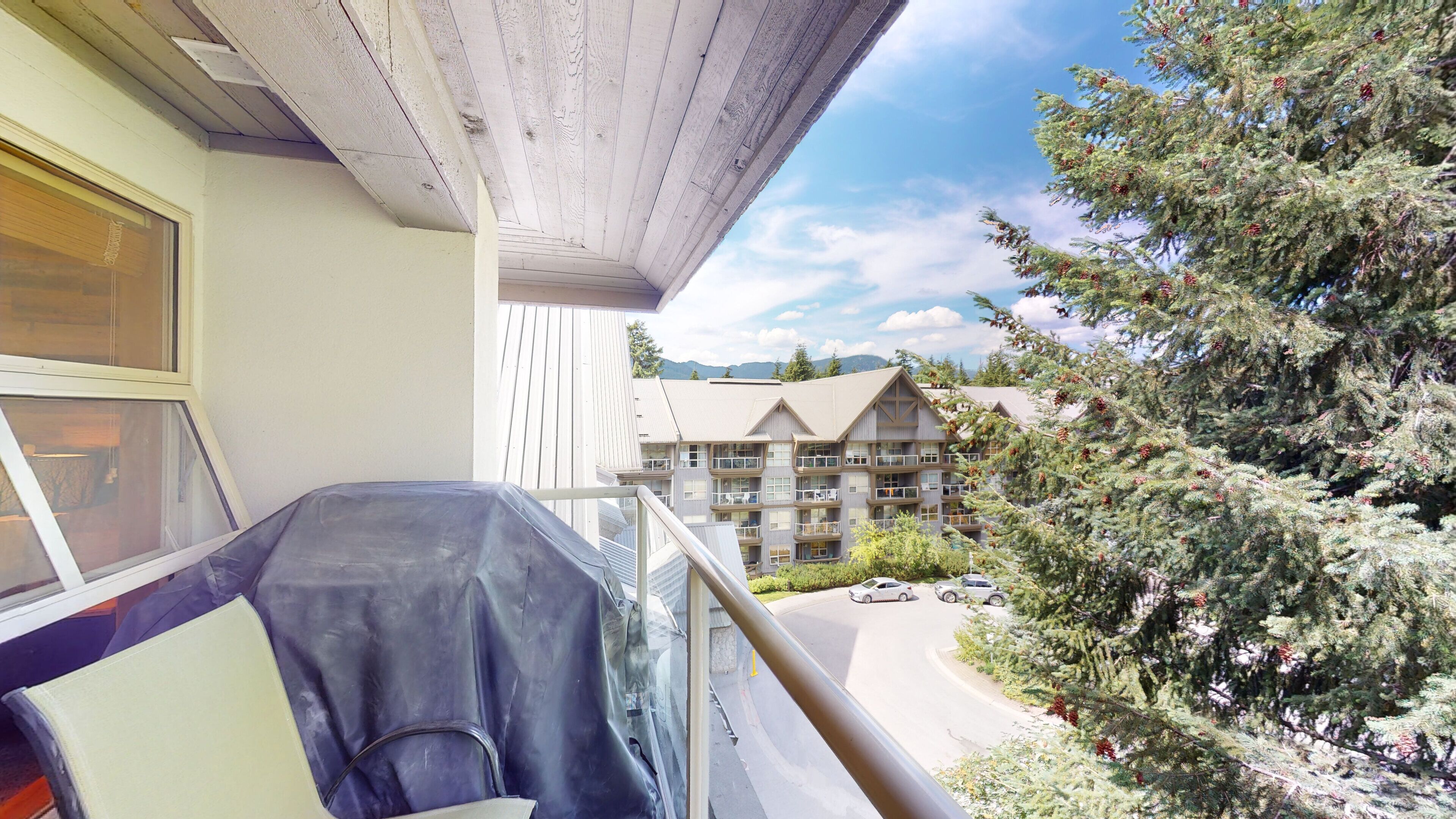 Un balcone con un'auto coperta, un edificio con diversi balconi e un albero con pigne.