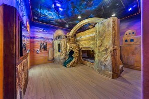 Un espace de jeux équipé d’un toboggan, d’un mur d’escalade et d’une fresque représentant une scène spatiale.