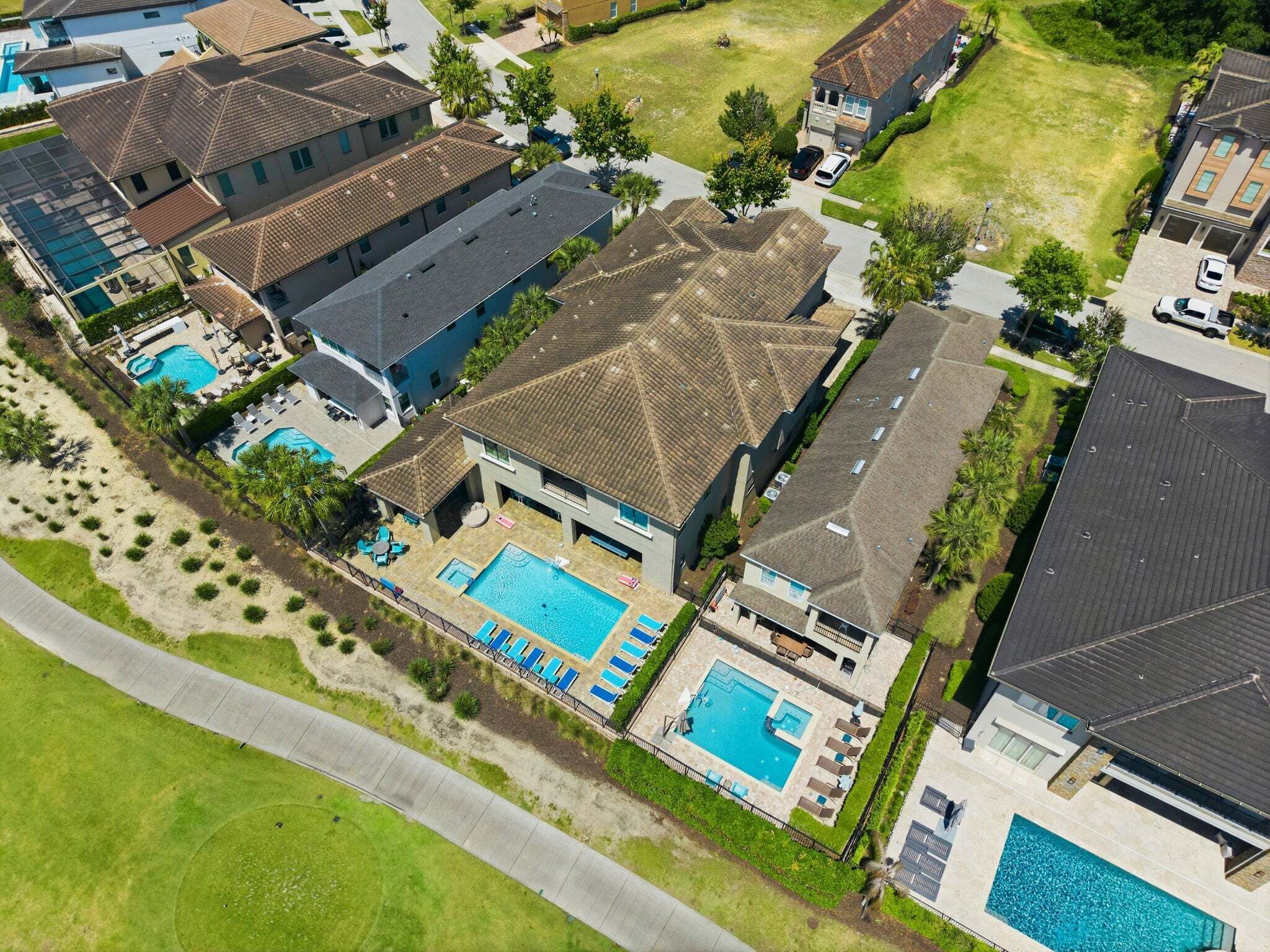 An aerial view of a residential area with multiple houses, a large swimming pool, and a beach area.