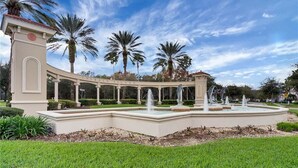 A landscaped area with a fountain, palm trees, and a building with a sign reading "Emerald Island". - ✦ 5min to Disney ✦ 6BR/5.5BA ✦ Private South Pool ✦ A/C Game Room ✦ Sleeps 14 (Kissimmee)