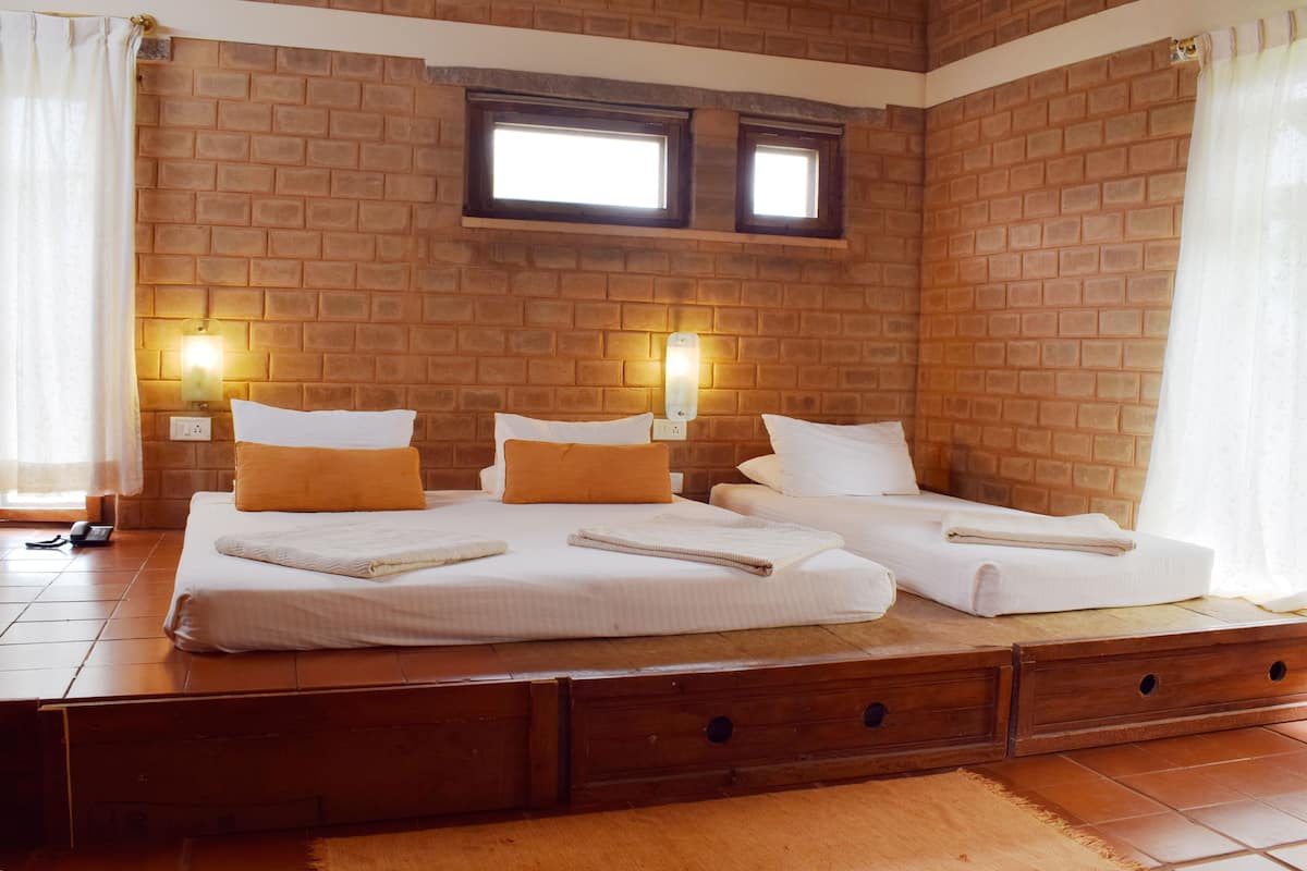 A room with two beds, a brick wall, two windows, and a wooden dresser.