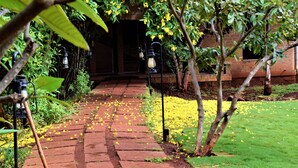 Un camino de ladrillo que lleva a la entrada de un edificio, rodeado de follaje y flores amarillas.