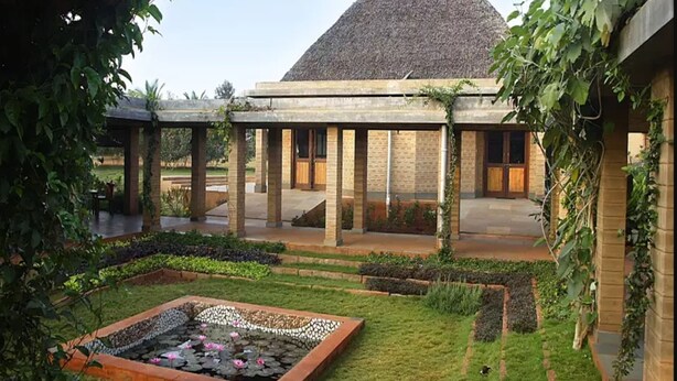 Un edificio con techo en forma de pirámide, un espacio al aire libre cubierto con columnas, y un jardín con un estanque.
