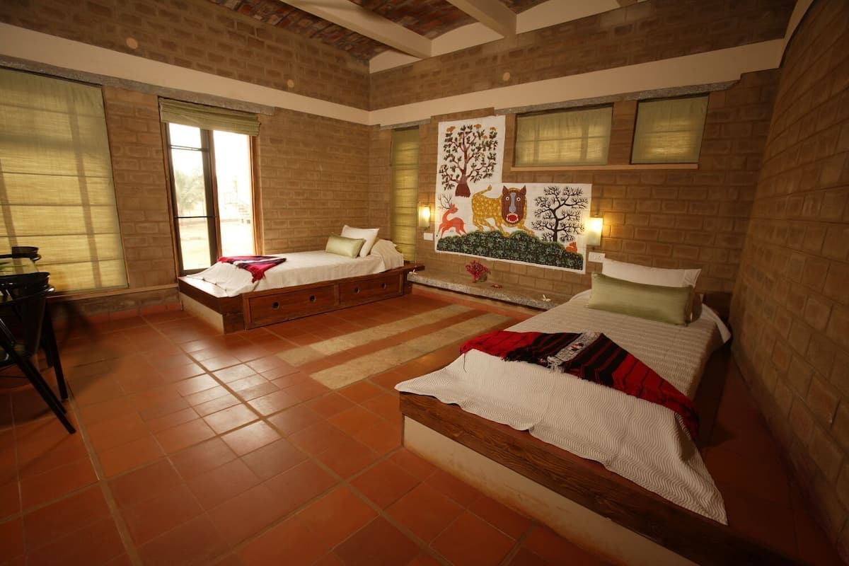 A bedroom with two beds, a wooden bench, a dining table, and a large mural on the wall.